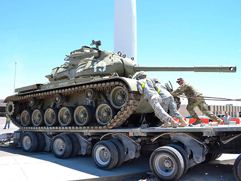 Several men positioning a US Army tank on top of a transporting vehicle outside of Fort Bliss and Old Ironsides Museums.